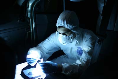 Un agente de Policía Científica recoge muestras en el interior de 
un vehículo con ayuda de la llamada luz forense. - DGP