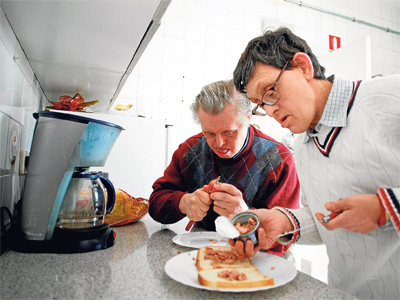 Fernando (izda.) y Miguel preparan un sándwich; abajo, Pepi elabora pulseras en la Fundación Gil Gayarre. - MÓNICA PATXOT