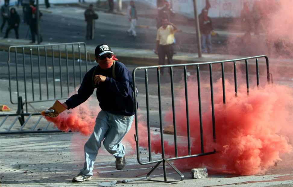 Un manifestante lanza una bomba de humo.