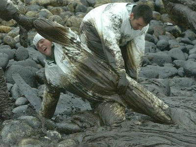 Dos personas extraen chapapote de la costa tras el hundimiento del Prestige. EFE