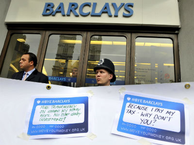 Un policía británico y un guardia de seguridad vigilan tras una pancarta donde los manifestantes pegan mensajes frente a una sucursal de Barclays. EFEAndy Rain