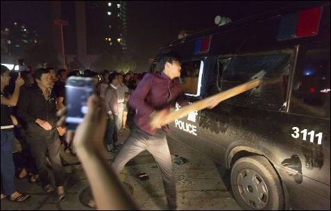 Un manifestante rompe el cristal de una camioneta de la Policía con un tablón de madera, durante una marcha en Yuyap (China). Protestan contra un informe de la televisión que, en su opinión, restó importancia a la situación provocada por el tifón Fitow.