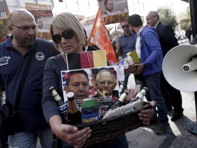 Una manifestante lleva una cesta con los retratos del ministro griego de Finanzas, izq), y de su homólogo alemán, junto con bebida y comida, a las puertas del Ministerio de Finanzas en Atenas, 17 de octubre de 2013. EFE/Alkis Konstantinidis