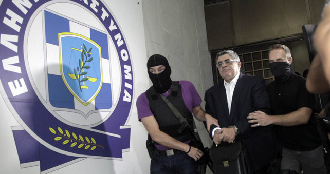 El líder de Amanecer Dorado, Nikolaos Mijaloliakos, esposado y custodiado por dos policías, es trasladado a dependencias judiciales tras su arresto el sábado.