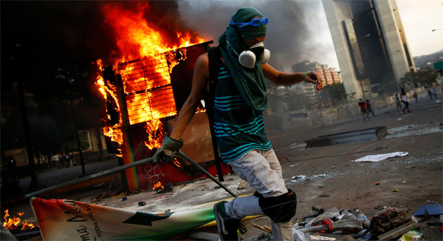 Un manifestante contrario al Gobierno de Maduro junto a un quisco de los trabajadores del metro de Caracas que fue incendiado durante protestas opositoras.