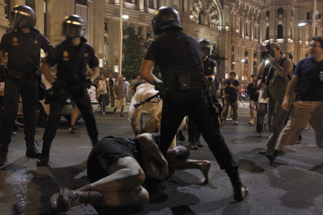 Un manifestante se agarra a la pierna de un antidisturbios durante las cargas policiales tras una manifestación en Madrid