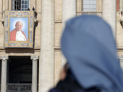 Una monja reza mientras unos trabajadores instalan un tapiz con la imagen del papa Juan Pablo II.- REUTERS