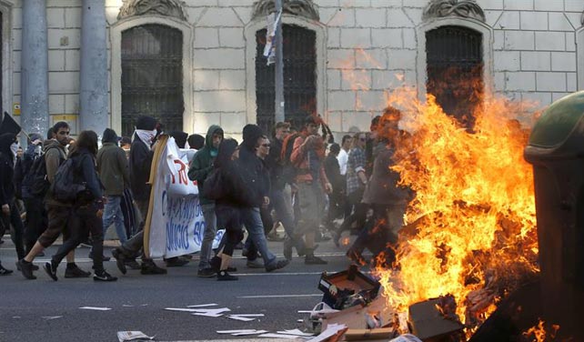 Participantes en una manifestación alternativa convocada esta tarde en Barcelona con motivo del 1 de mayo pasan ante un contenedor ardiendo.