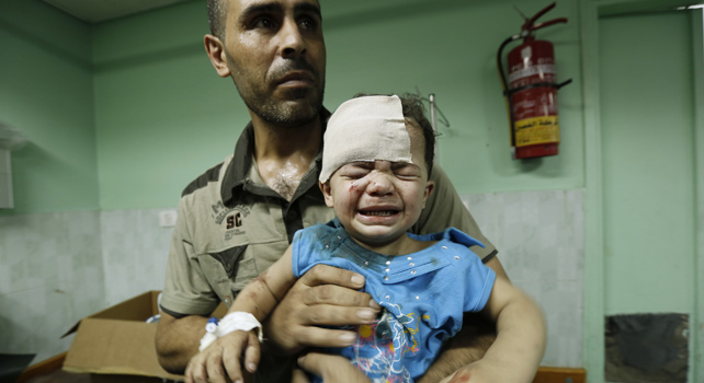 Un hombre coge en brazos a un niño herido tras el ataque de Israel a una escuela de la ONU.