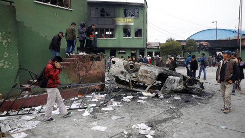 Ciudadanos caminan junto a un coche calcinado en El Alto, Bolivia. / Reuters