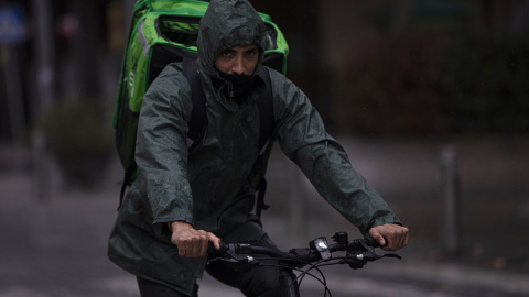 Un rider (repartidor) trabaja bajo la lluvia protegido con un impermeable, en Sevilla . E.P./María José López