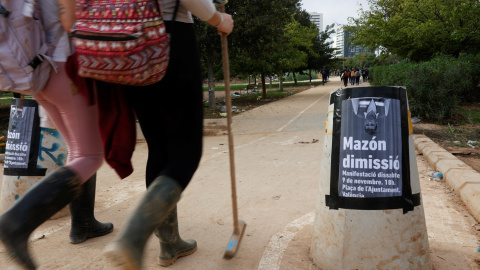 Dos voluntarios en las tareas de reconstrucción tras la DANA pasan junto a un cartel que llama a una manifestación en protesta por la gestión del president de la Generalitat Valenciana, Carlos Mazón, en València. REUTERS/Eva Manez