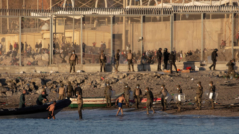  Miembros del ejército ayudan a dos inmigrantes a su llegada a la playa de El Tarajal, junto a la valla fronteriza , en Ceuta este miércoles.- EFE