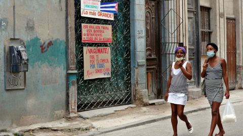  Dos mujeres caminan junto a varios carteles expuestos en la ventana de una casa en una calle de La Habana, Cuba, este martes 20 de julio del 2021. EFE/ Ernesto Mastrascusa