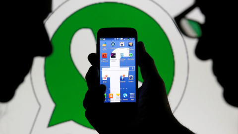 Foto que muestra un hom,bnre sosteniendo un móvil con el logo de Facebook en la pantalla, y detrás, el logo de logo de WhatsApp. REUTERS/Dado Ruvic