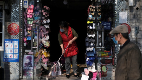 Una mujer con mascarilla limpia la entrada de su tienda en Pekín.. REUTERS/Carlos Garcia Rawlins