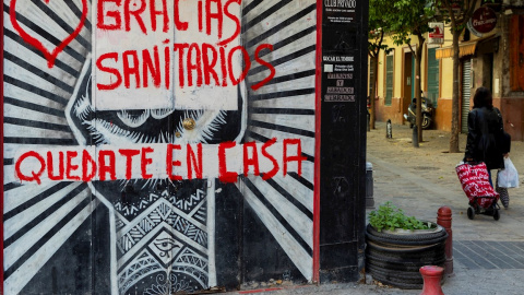 Una mujer con un carro de la compra pasa junto a un comercio cerrado con una pintada de agradecimiento a los sanitarios en una céntrica calle de Sevilla, hoy miércoles en la séptima semana de confinamiento decretado en el Estado de Alarma debido a la c