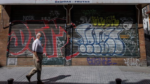 Un hombre protegido con mascarilla camina ante un comercio cerrado en una céntrica calle de Sevilla, durante el confinamiento decretado en el Estado de Alarma debido a la crisis sanitaria de la covid-19. EFE/Julio Muñoz