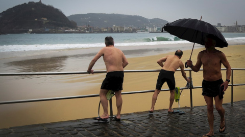 Varios hombres se bañan este martes en la playa de Ondarreta de San Sebastián a pesar del frío y la lluvia. EFE