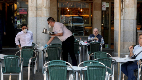 25/05/2020.- Un camarero sirve a los clientes en su bar de la Plaza Mayor de Salamanca este lunes durante el primer día de la fase 1 en la ciudad cuando las terrazas de los bares tienen su capacidad al 50 % y se permite el acceso a los grandes parques. E