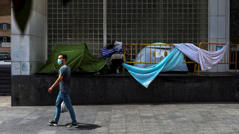 Un home passa davant de diverses tendes de campanyes de persones sense llar, aquest dimecres al centre de Barcelona. EFE/ Enric Fontcuberta