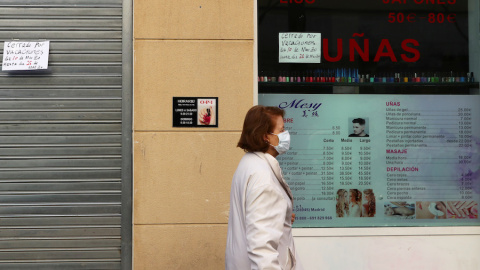 Una mujer usa una mascarilla mientras pasa por una peluquería cerrada propiedad de residentes chinos en Madrid. REUTERS / Sergio Perez