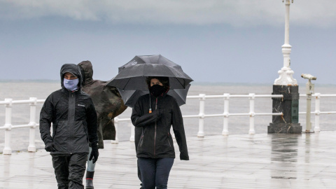 Un grupo de personas paseando por la playa de San Lorenzo de Gijon, bajo un fuerte chubasco y viento - EFE/Alberto Morante