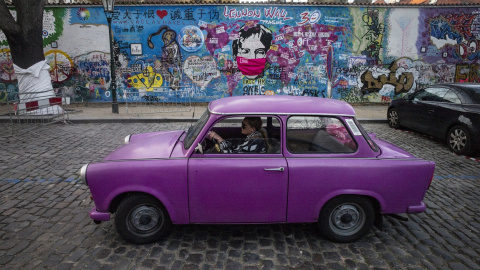 Una mujer con mascarilla conduce un coche violeta junto al llamado Muro de John Lennin, en el centro histórico de Praga. AFP/Michal Cizek