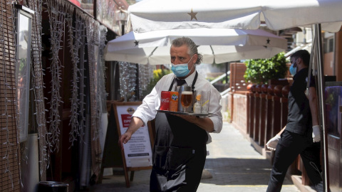 27/05/2020.- Un camarero lleva su pedido a unos clientes a una de las terrazas del Puerto Olímpico de Barcelona. / EFE