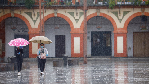 Dos mujeres con mascarillas y paraguas caminan por Córdoba. EFE/Salas