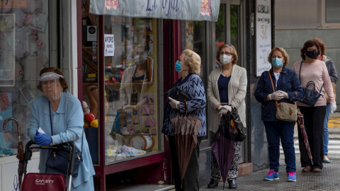 12/05/2020.- Varias mujeres con mascarillas hacen cola ante una mercería en el barrio de Triana de Sevilla, hoy martes en el segundo día de la fase 1 de desescalada en la que diferentes actividades han podido retomar su actividad desde que se inició el