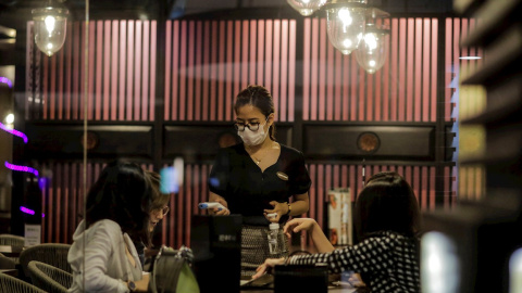 Una camarera con mascarilla atiende a unos clientes en un restaurante de Singapur. EFE/EPA/WALLACE WOON