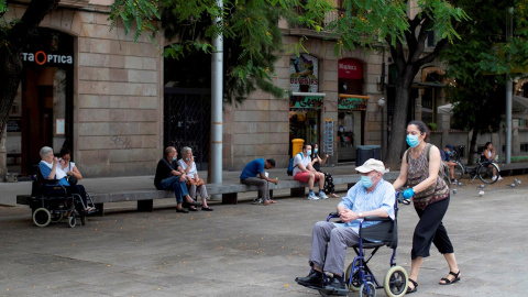 Una mujer empuja la silla de un anciano en el centro de Barcelona.  - EFE