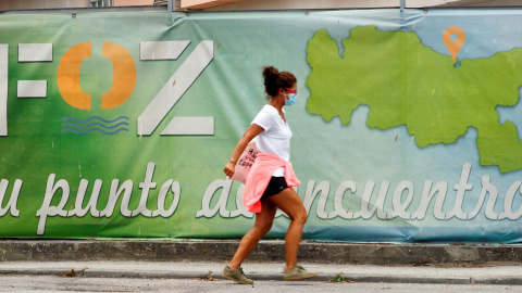 Una mujer con mascarilla camina frente a un cartel publicitario del pueblo de A Mariña, este miércoles en Lugo. | EFE