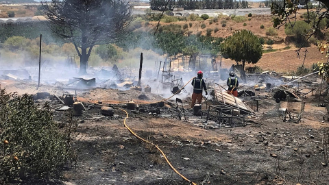 Miembros de los servicios de bomberos extinguen las llamas tras un incendio declarado en un asentamiento chabolista de Lepe, Huelva. - EFE