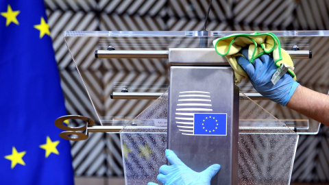 Un operario desinfecta un atril con la bandera de la UE, antes de la rueda de prensa del presidente del Consejo Eureopeo, Charles Michel. tras la primera cumbre de la UE en la se comenzaron a discutir el plan contra la crisis del coronavirus.. REUTERS/Fra