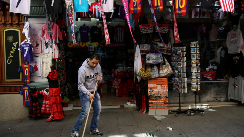 El empleado de una tienda de objetos turísticos del centro de Madrid barre la acera. REUTERS/Susana Vera