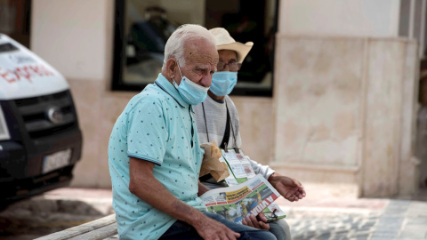 Una pareja de ancianos se protegen con mascarillas mientras descansan en un banco en Mahón, este jueves. | EFE