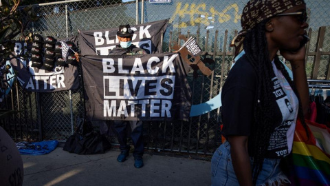 Un hombre (L) con una máscara facial vende banderas y otros accesorios con el eslogan 'Black Lives Matter'