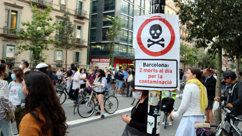 Primer pla d'un cartell que diu que la contaminació mata amb una manifestació contra els cotxes darrere, al centre de Barcelona. ACN / Pol Solà