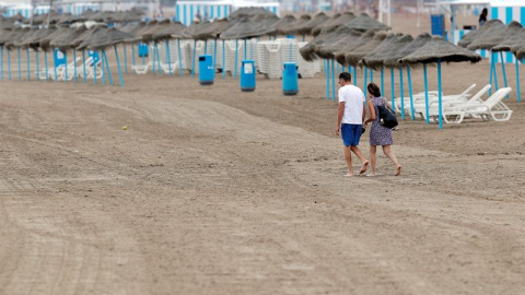 Una pareja pasea por la playa de la Malvarrosa en la que la afluencia de gente ha descendido notablemente debido en gran medida al descenso de temperaturas, a los chubascos y al cielo nublado. /EFE