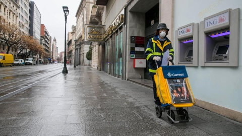 Una trabajadora del servicio de Correos realiza su trabajo por las calles casi desiertas de Zaragoza el pasado lunes. EFE/Javier Cebollada