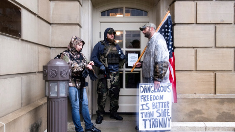 Manifestantes contra las medidas de confinamiento decretadas por el gobernador de Michigan, Gretchen Whitmer, se refugian de la lluvia en una de las entradas del Capitolio del Estado, en la localidad de Lansing. REUTERS/Seth Herald