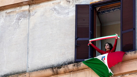 Una mujer luce la bandera italiana desde su ventana para celebrar el 75 aniversario de la liberación italiana, durante el confinamiento decretado por pandemia del coronavirus.- efe