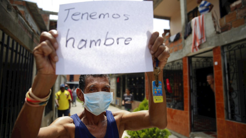 Un hombre es visto con un cartel mientras protesta este jueves en Cali (Colombia). Decenas de personas salieron de sus casas haciendo sonar cacerolas para reclamar a la alcaldía por la falta de ayudas y alimentos en medio de la cuarentena por la emergenc