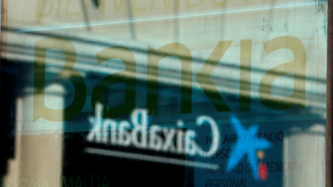 El logo de una oficina de Caixabank se refleja en el ventanal de una sucursal de Bankia en Barcelona. REUTERS