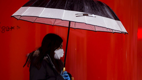 Una mujer camina bajo la lluvia con mascarilla y guantes en Málaga, durante la novena jornada de confinamiento tras decretarse el Estado de Alarma. EFE/Jorge Zapata