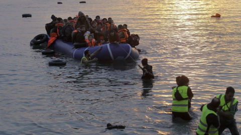 Voluntarios de una ONG ayudan a refugiados y migrantes que llegan en una lancha neumática a la costa de Mytilini, en la isla de Lesbos (Orestis Panagiotou / EFE)