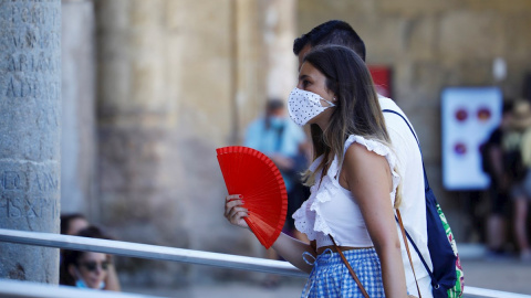 Una mujer protegida con unas mascarilla mientras se abanica para aliviar las altas temperaturas de este jueves en Córdoba. | EFE