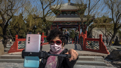 Una mujer con mascarilla se hace un selfi frente al Palacio de Verano de Pekín. China vuelve poco a poco a recuperar la normalidad tras dos meses de confinamiento por el coronavirus.